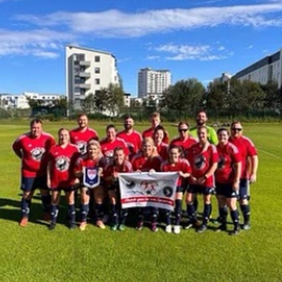 A senior team in red lined up behind their club banner