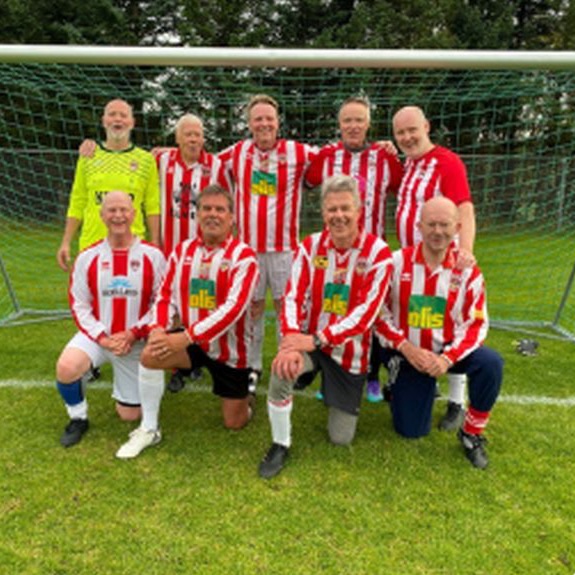A senior team in red and white stripes posing in front of the goal