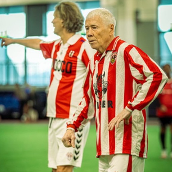 Two veteran players in red and white striped shirts on an indoor pitch