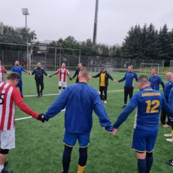 Walking Football players holding hands in a circle on the pitch