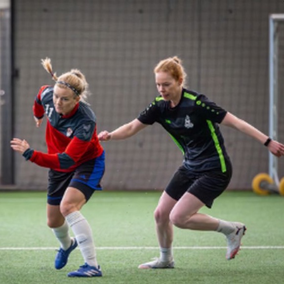 Two women battling for the ball on an indoor pitch